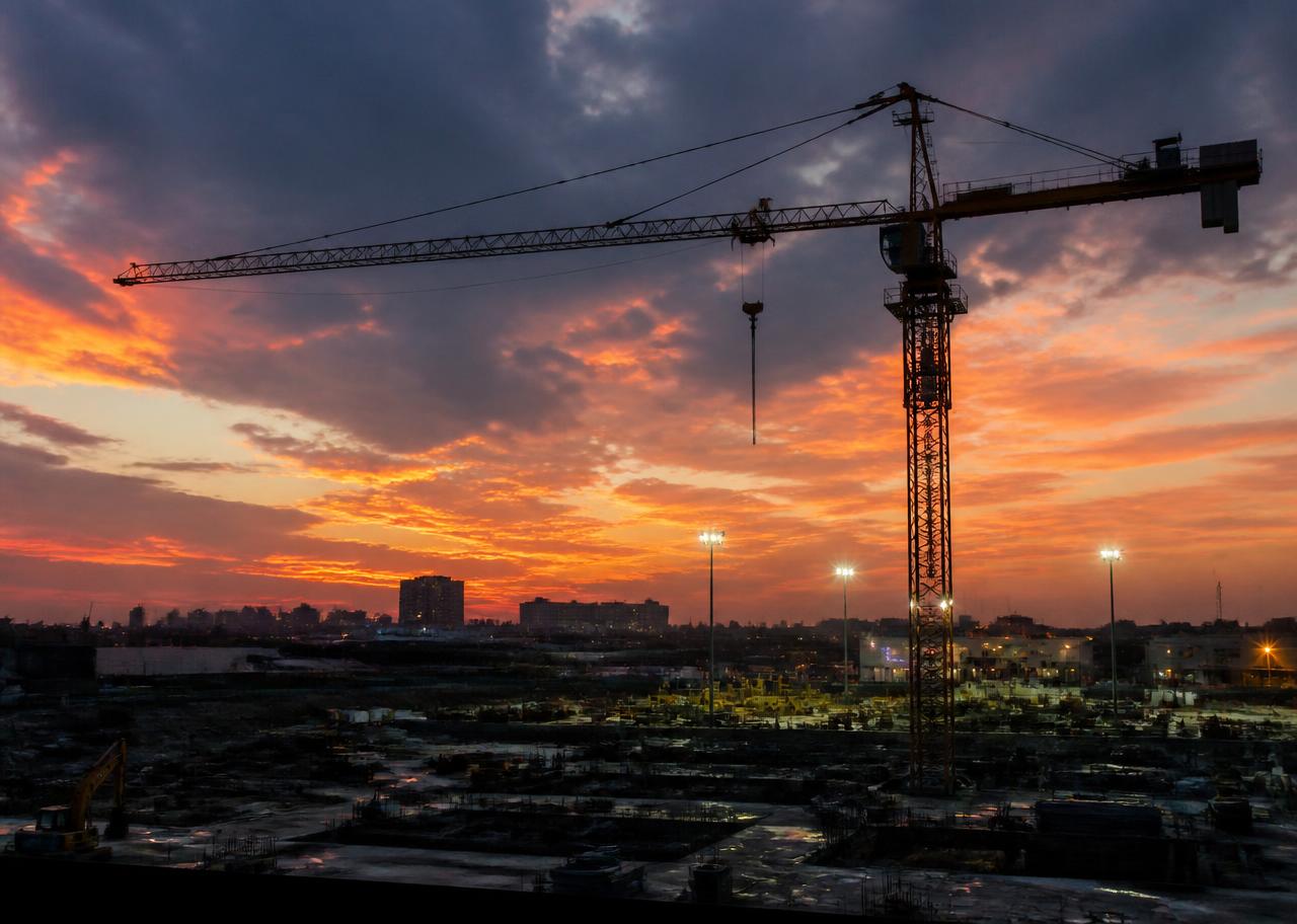 Tower crane silhouette against a dusk sky over a construction site